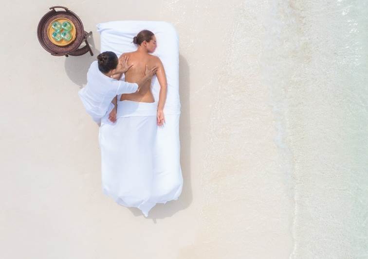 Guest enjoying a relaxing private wellness massage on the beach at Naladhu Private Island Maldives